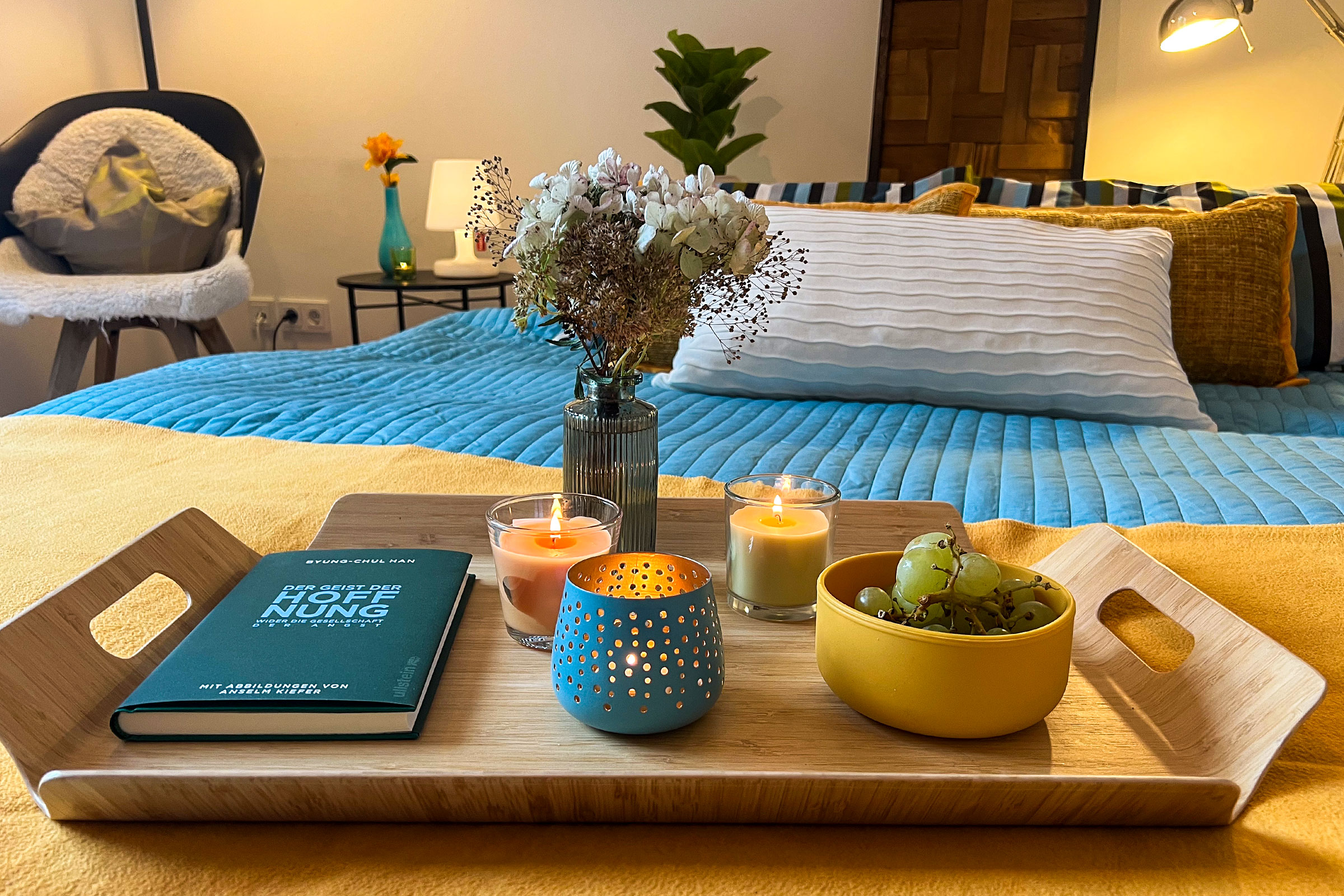 Ein Tablett mit Büchern, Kerzen und einer Vase auf einem Bett
